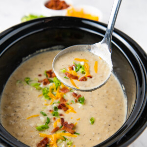 a ladle with crockpot baked potato soup over a slow cooker with soup