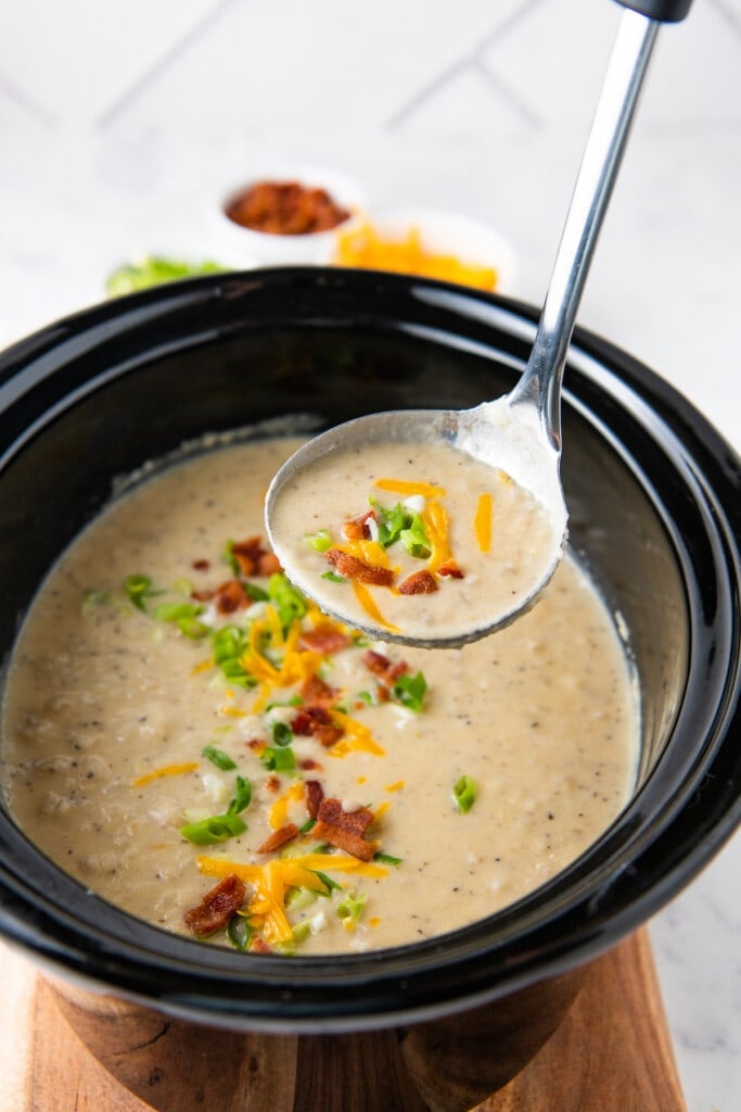 a ladle with crockpot baked potato soup over a slow cooker with soup