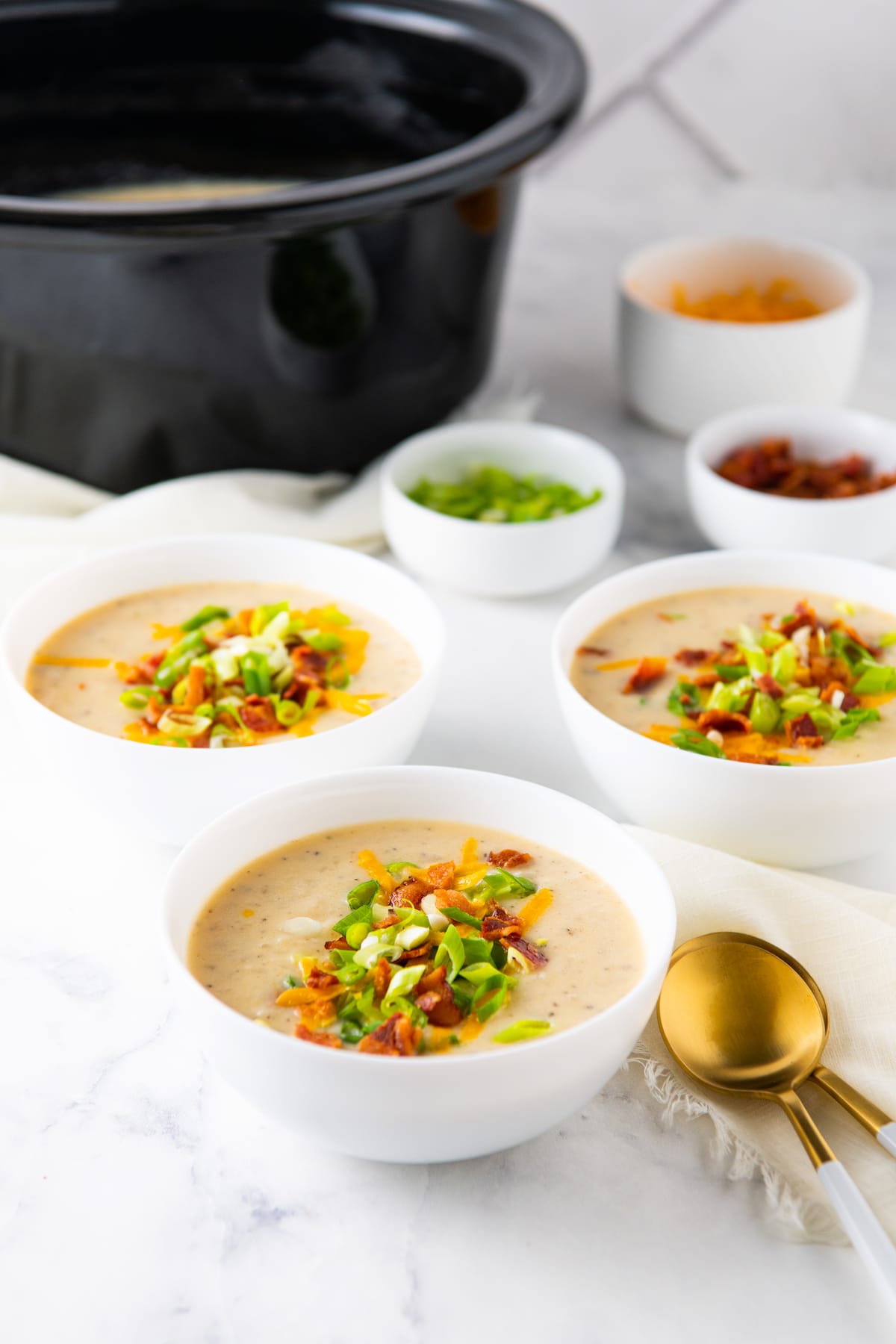 three bowls of crockpot baked potato soup with garnishes