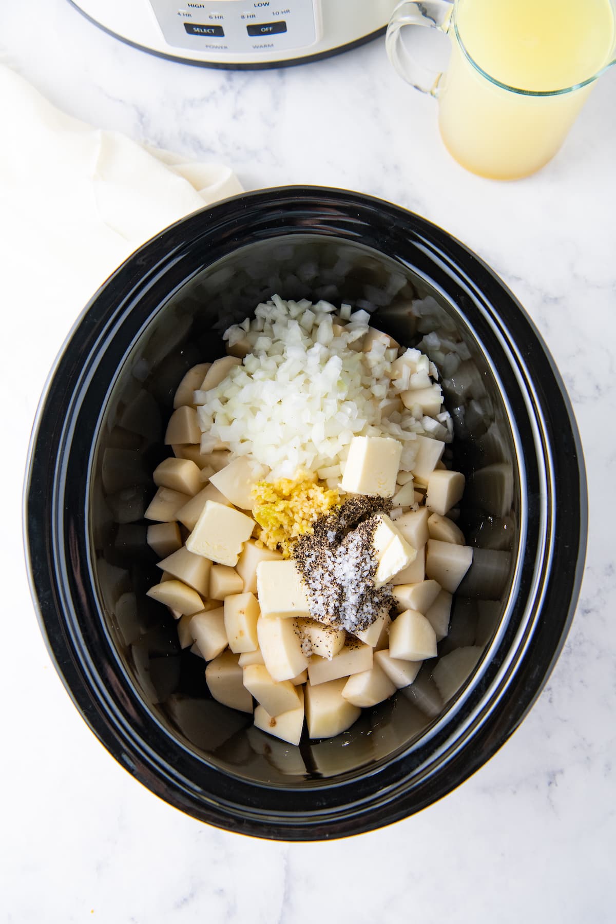a crockpot with potatoes, onions, butter, and seasonings