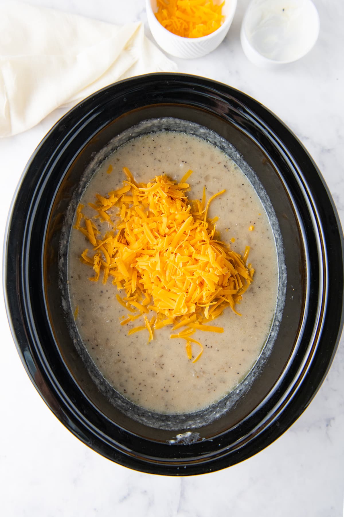 adding cheese to a crockpot with creamy soup