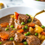 a bowl of crockpot beef stew with a spoon taking a bite out of the bowl
