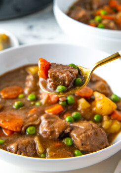 a bowl of crockpot beef stew with a spoon taking a bite out of the bowl