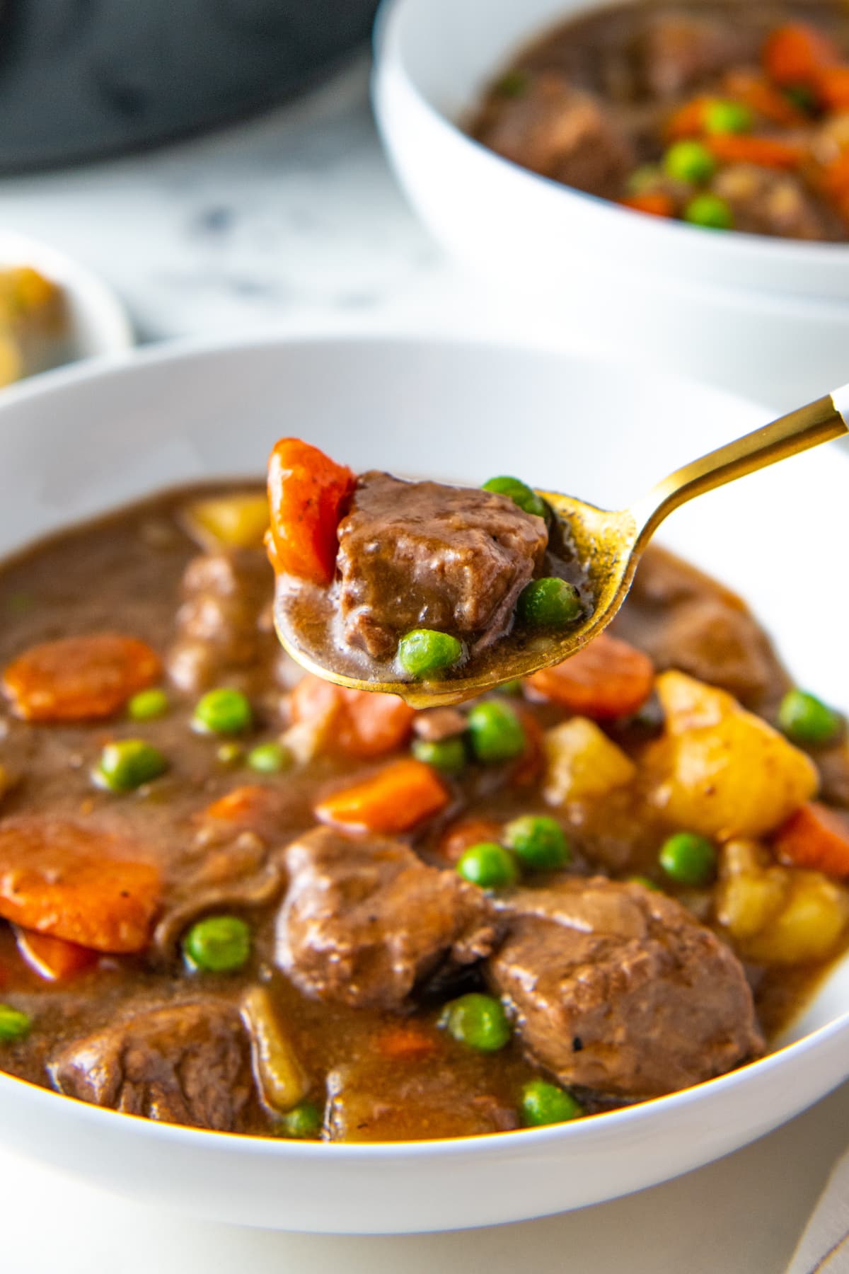 a bowl of crockpot beef stew with a spoon taking a bite out of the bowl