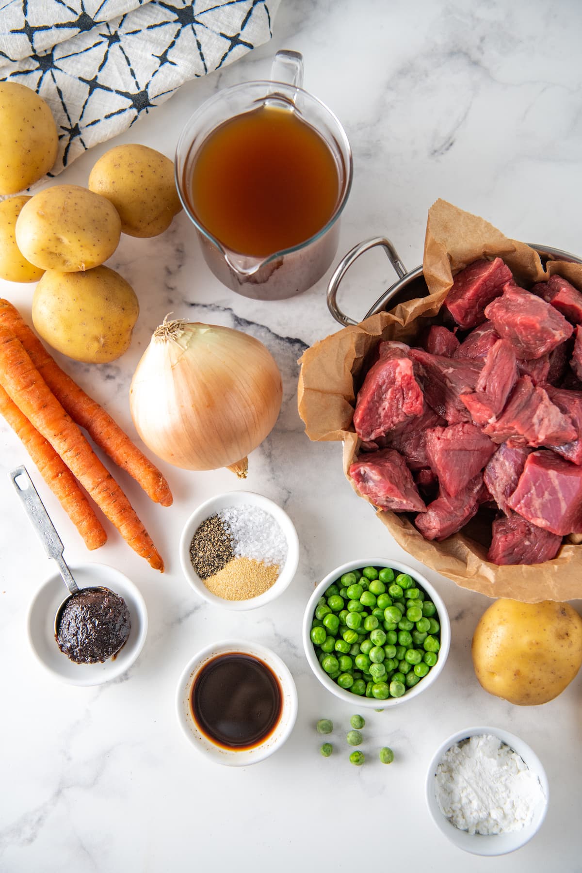 ingredients to make beef stew like beef chunks, carrots, peas, onions, potatoes, and seasonings