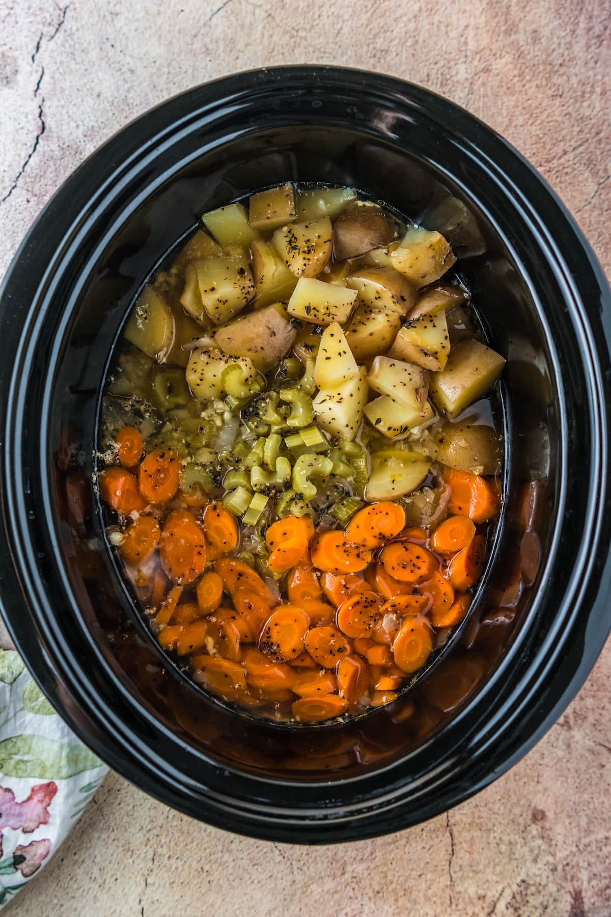 a crockpot with carrots, celery, potatoes, and broth