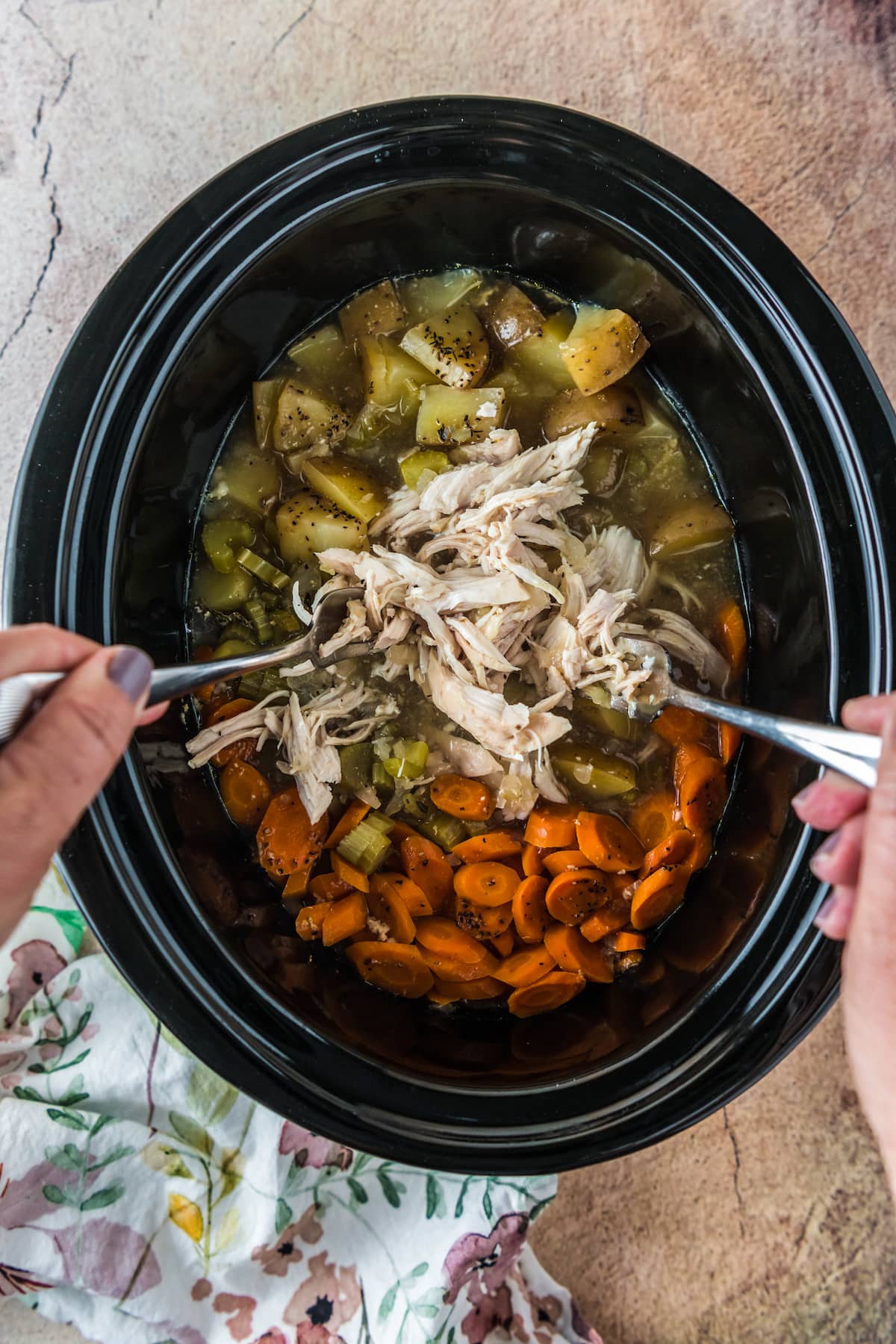 shredding chicken in a crockpot with broth, carrots, and potatoes