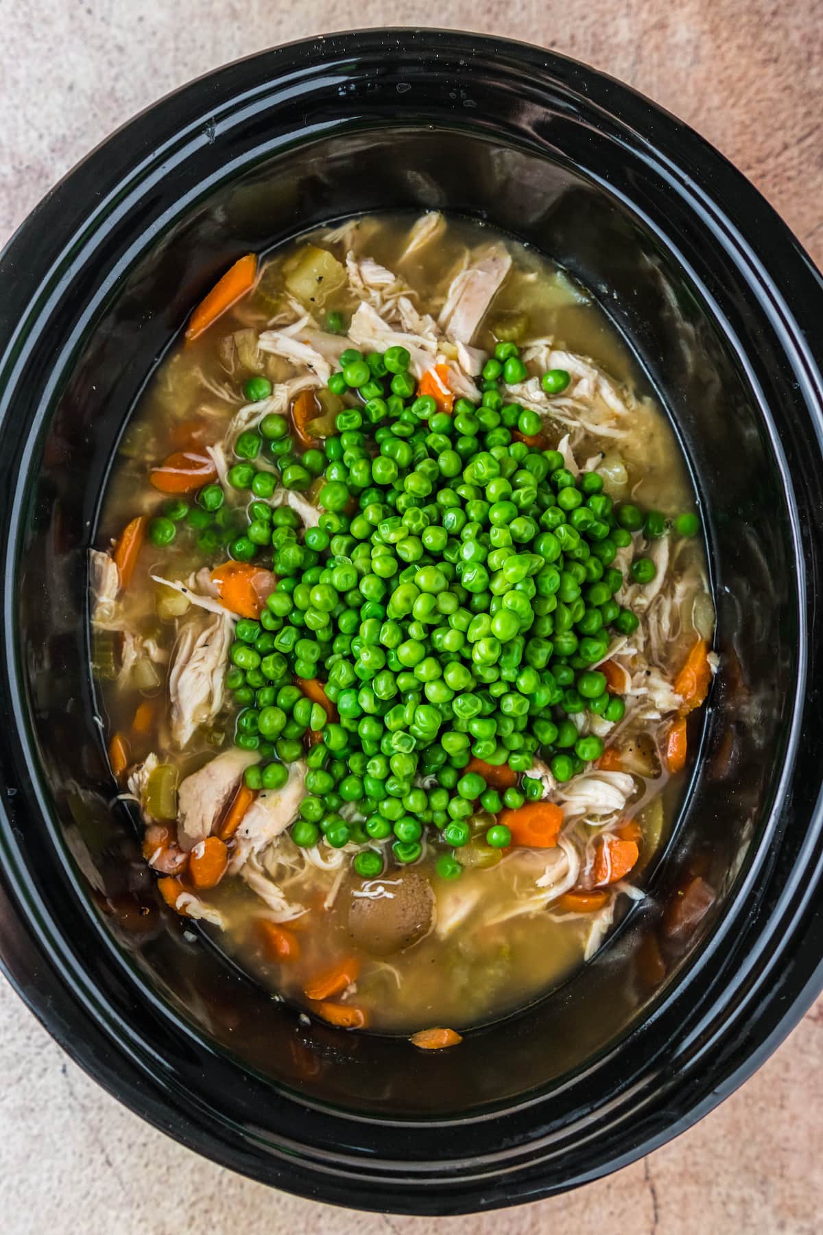 a large portion of peas in a crockpot with chicken, carrots, and potatoes