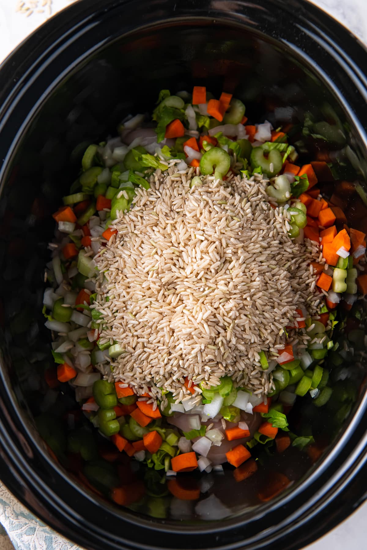 rice poured over diced vegetables in a crockpot