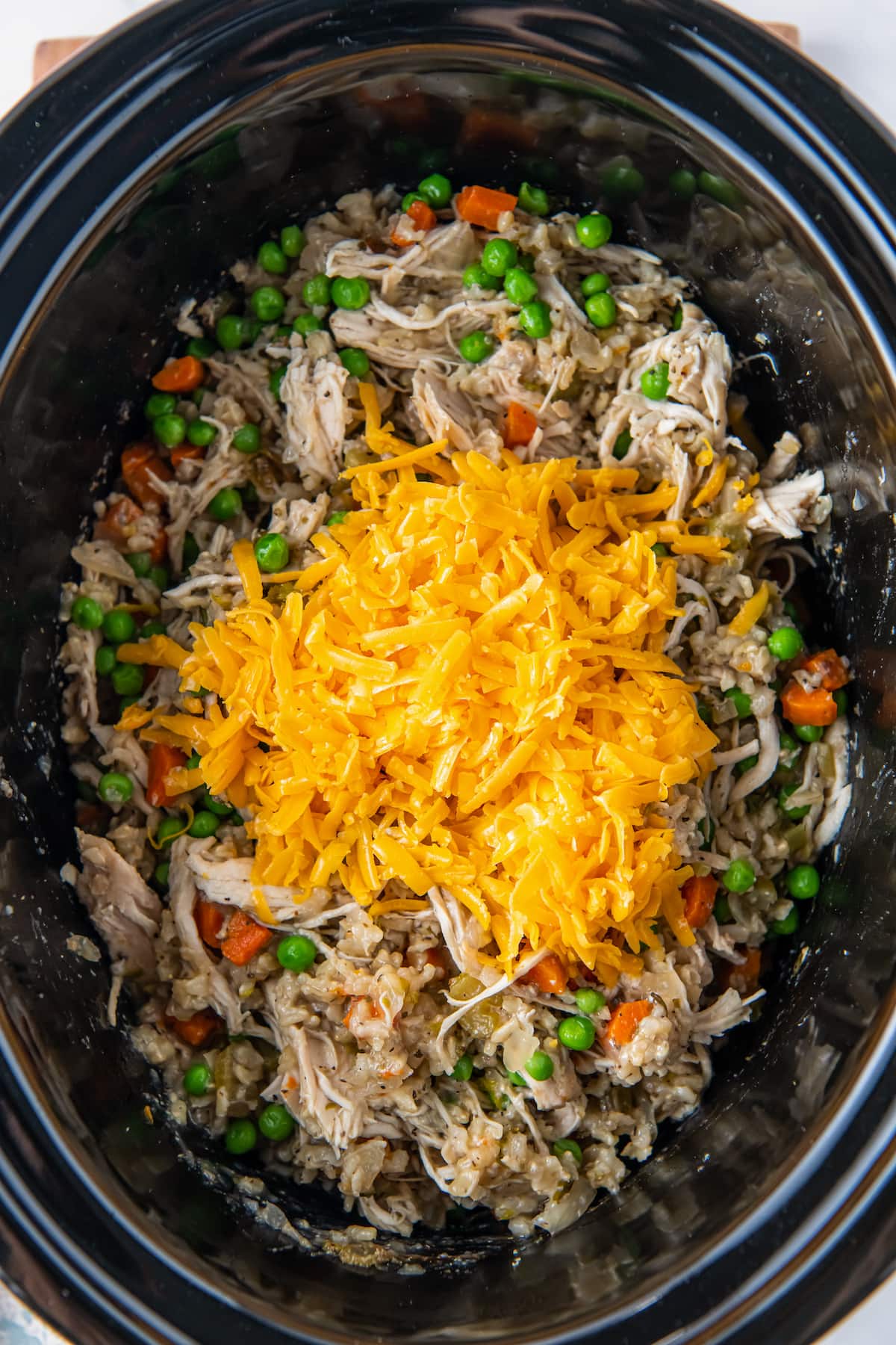 shredded cheese on top of chicken, rice, and vegetables in a crockpot