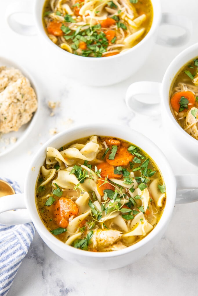 Three bowls of homemade chicken noodle soup with egg noodles and s side of crusty bread. 