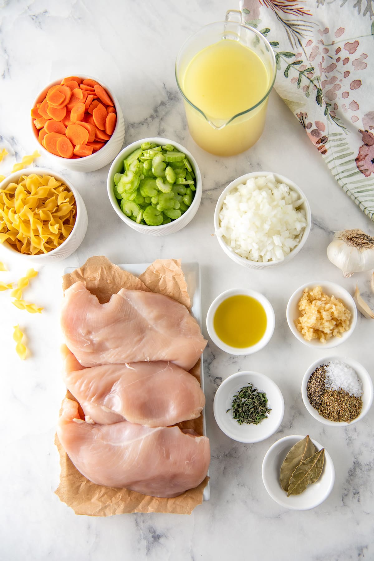 ingredients to make chicken noodle soup including chicken breasts, diced carrots, celery, and onions, and other seasonings