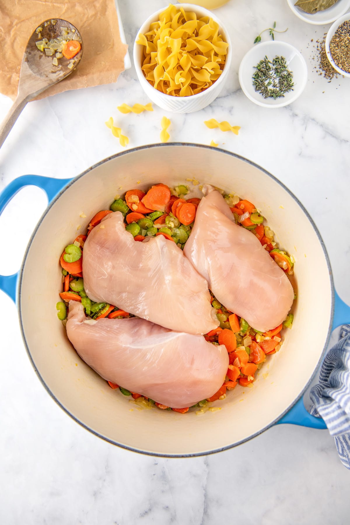 Three raw chicken breasts are placed on top of chopped veggies in a dutch oven. 