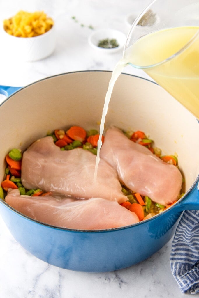pouring stock over chicken breasts and vegetables in a dutch oven