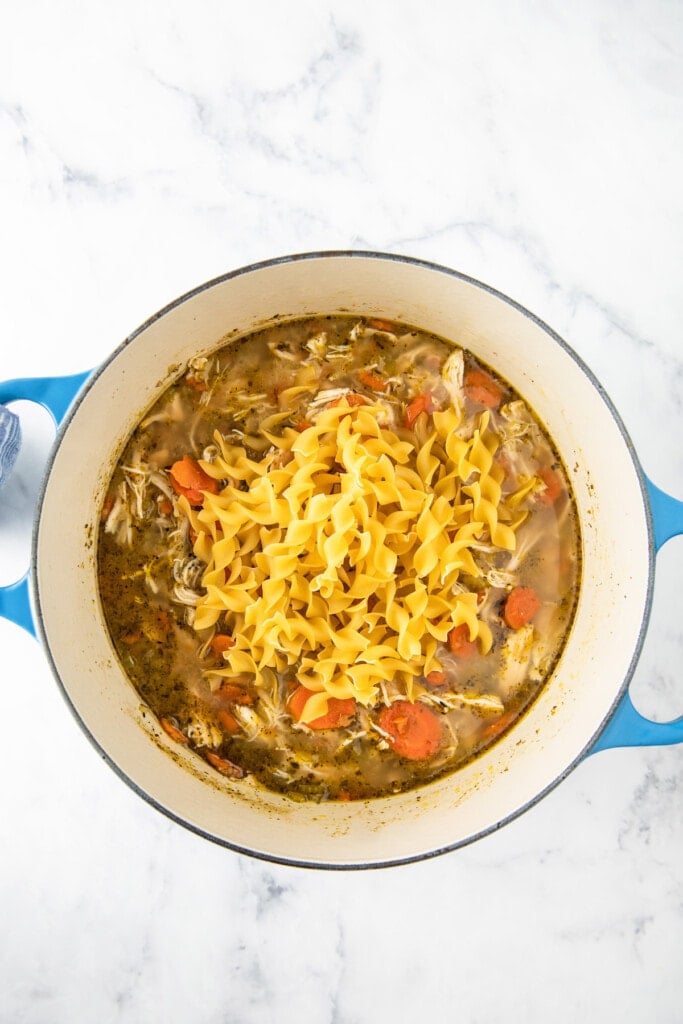 adding noodles to soup in a large dutch oven