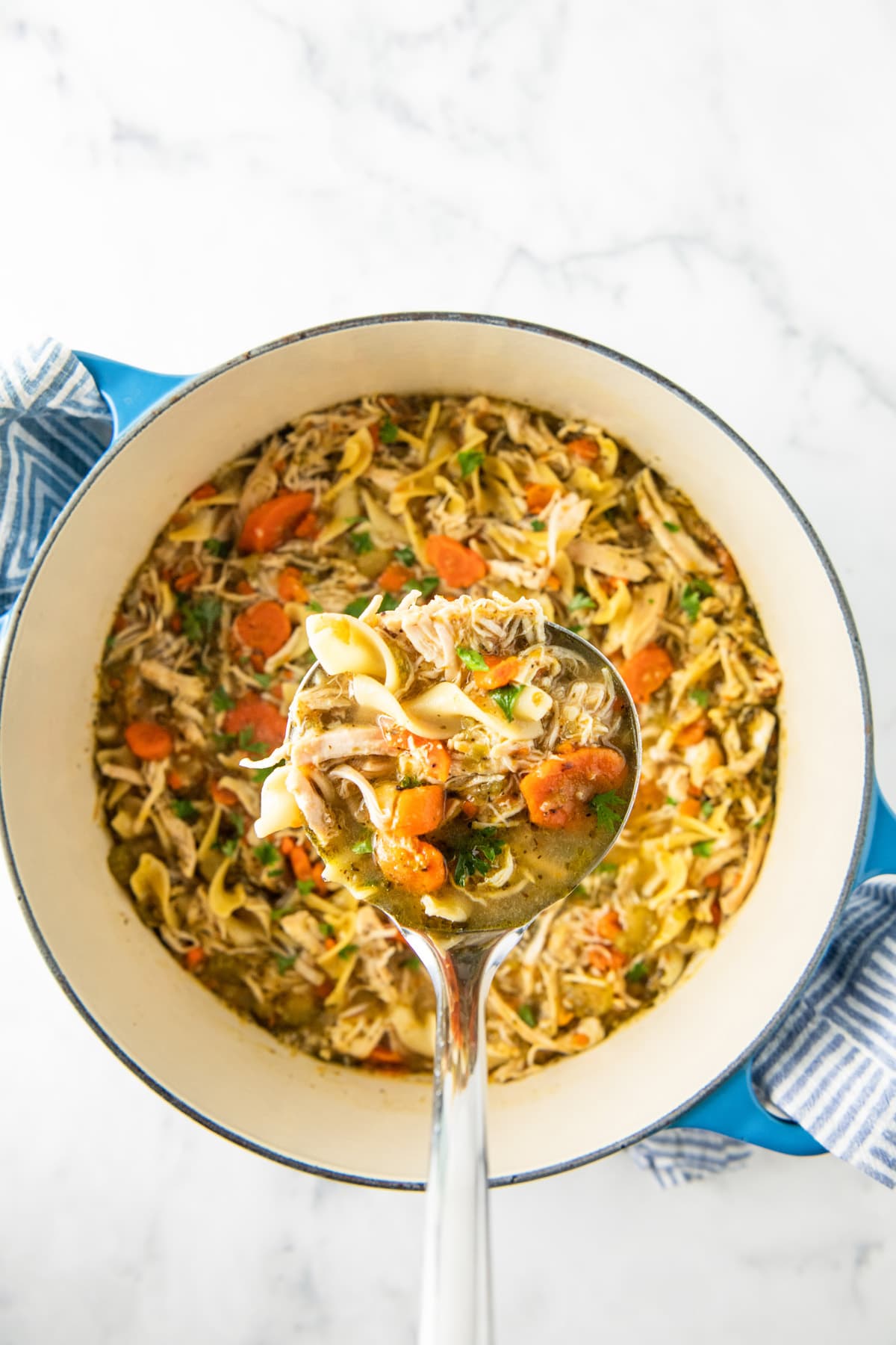 a ladle of chicken noodle soup over a dutch oven