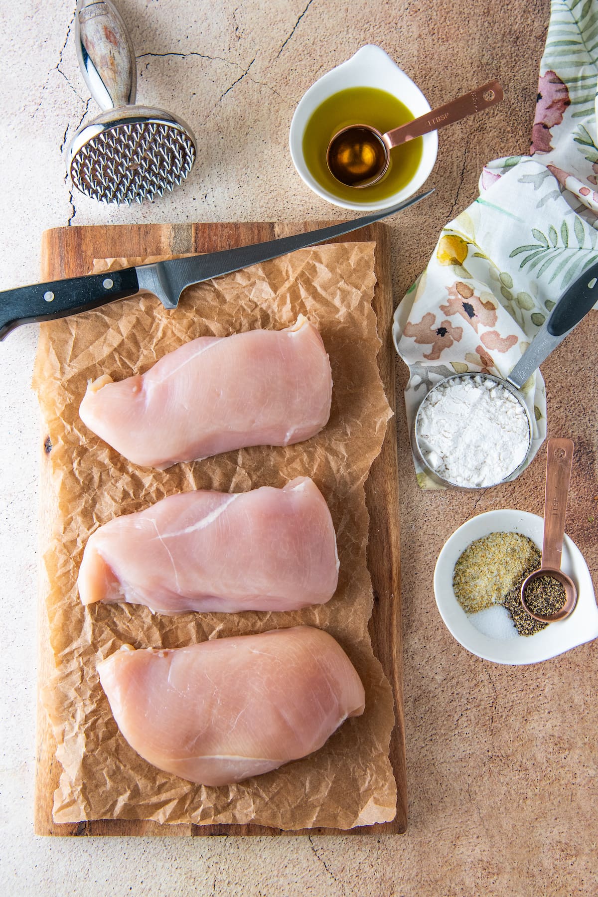 a cutting board with chicken breasts alongside flour and seasonings