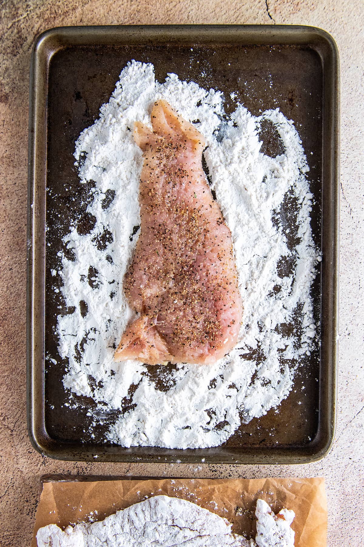 a chicken breast on top of flour on a sheet tray