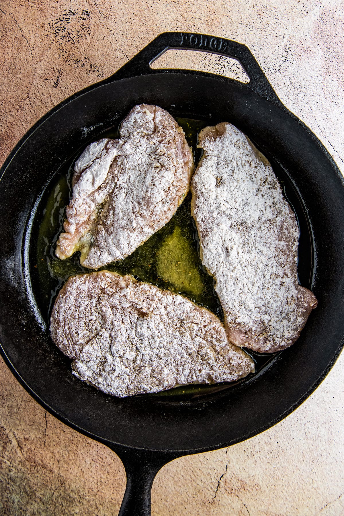 three floured pieces of chicken in a skillet