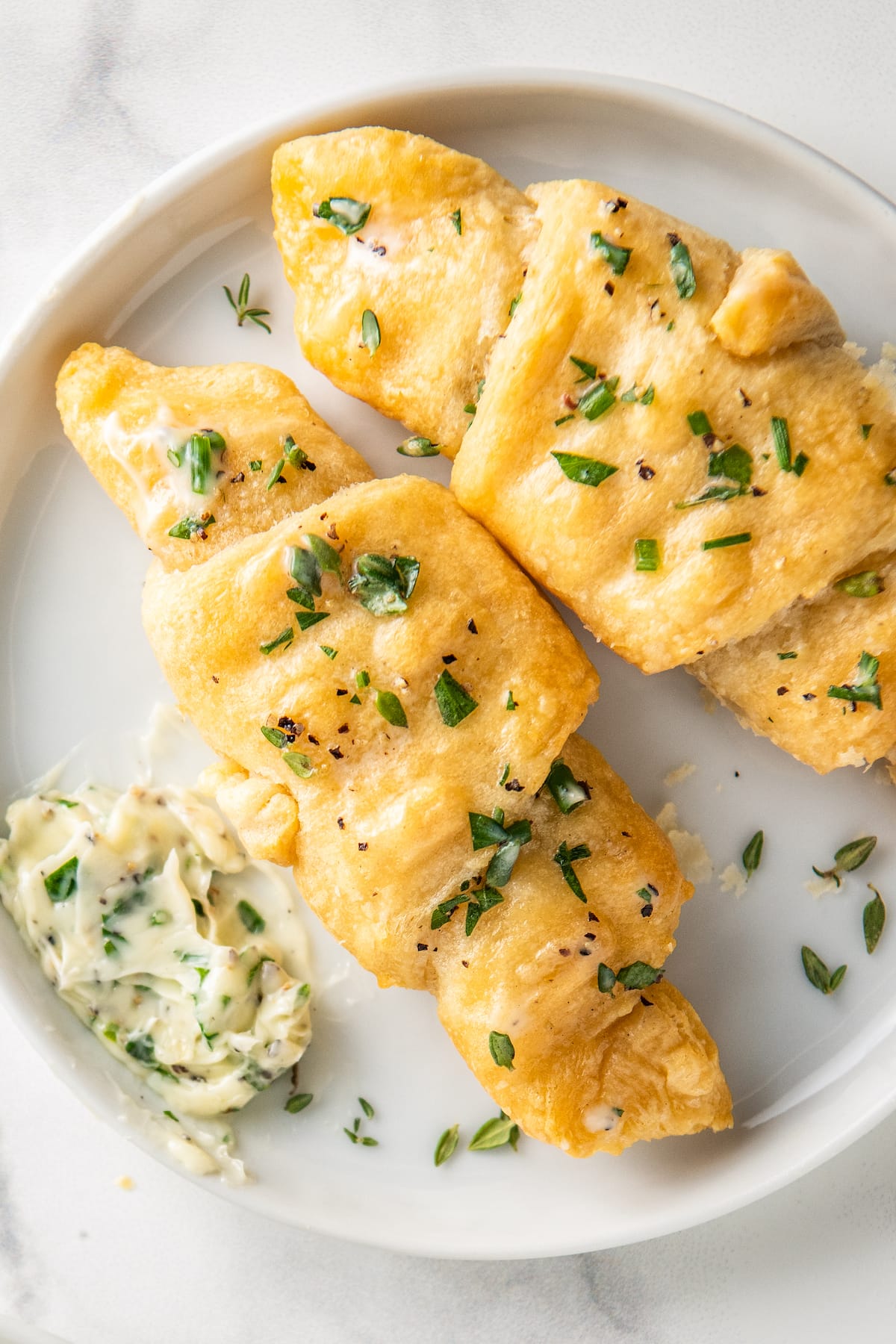crescent rolls on a plate with herbs and next to herb butter