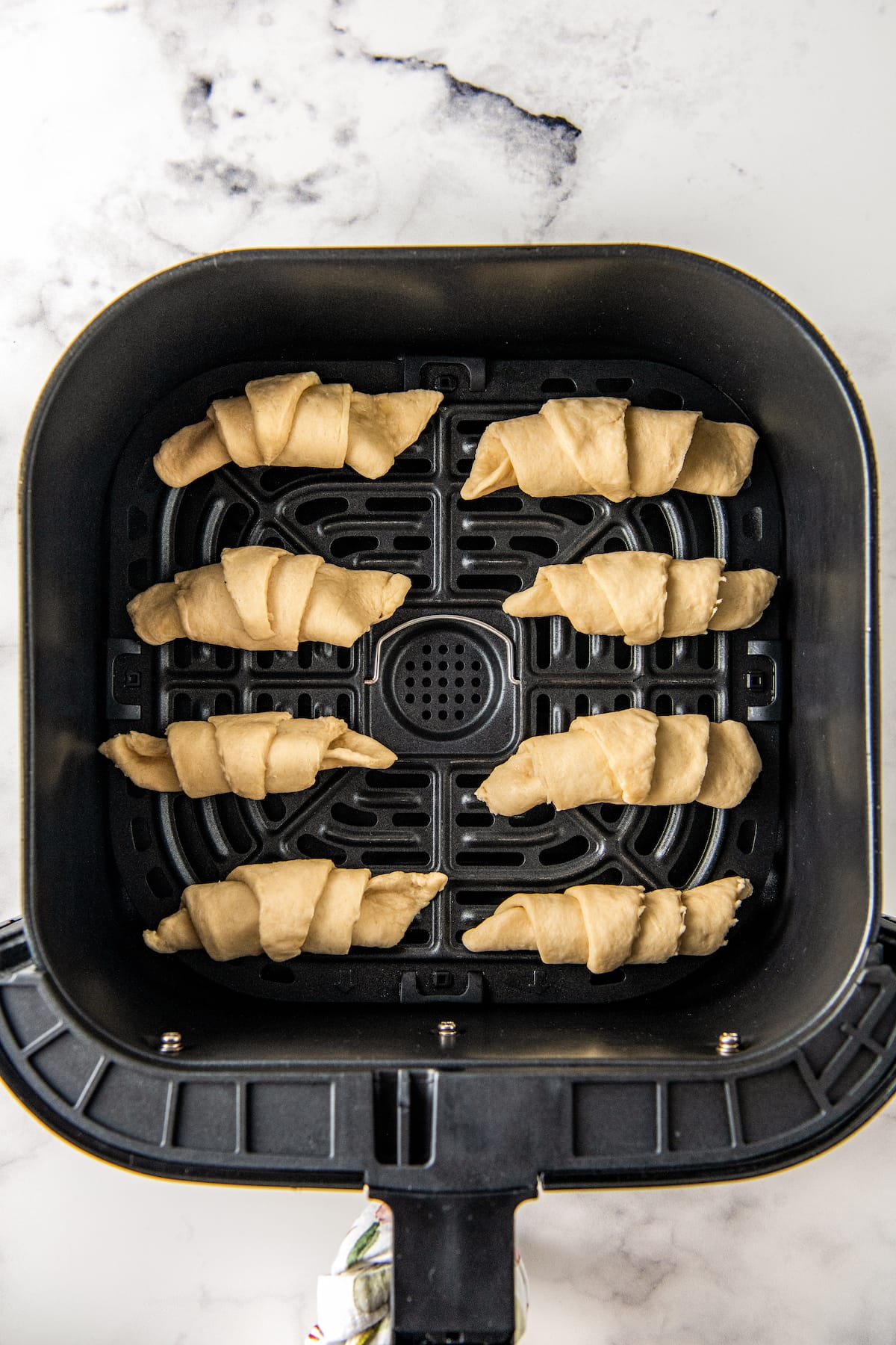 eight uncooked rolls in an air fryer tray