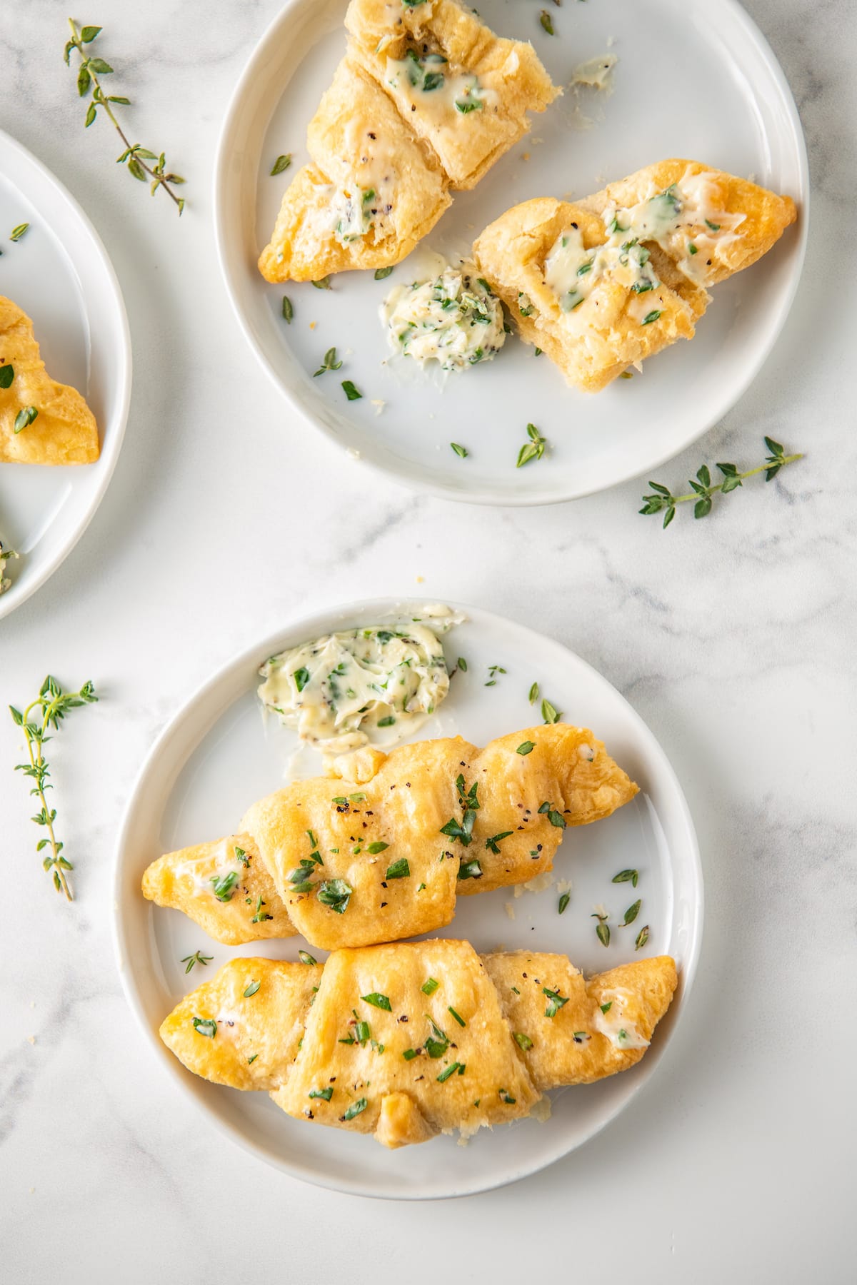 crescent rolls on a plate with herbs and next to herb butter