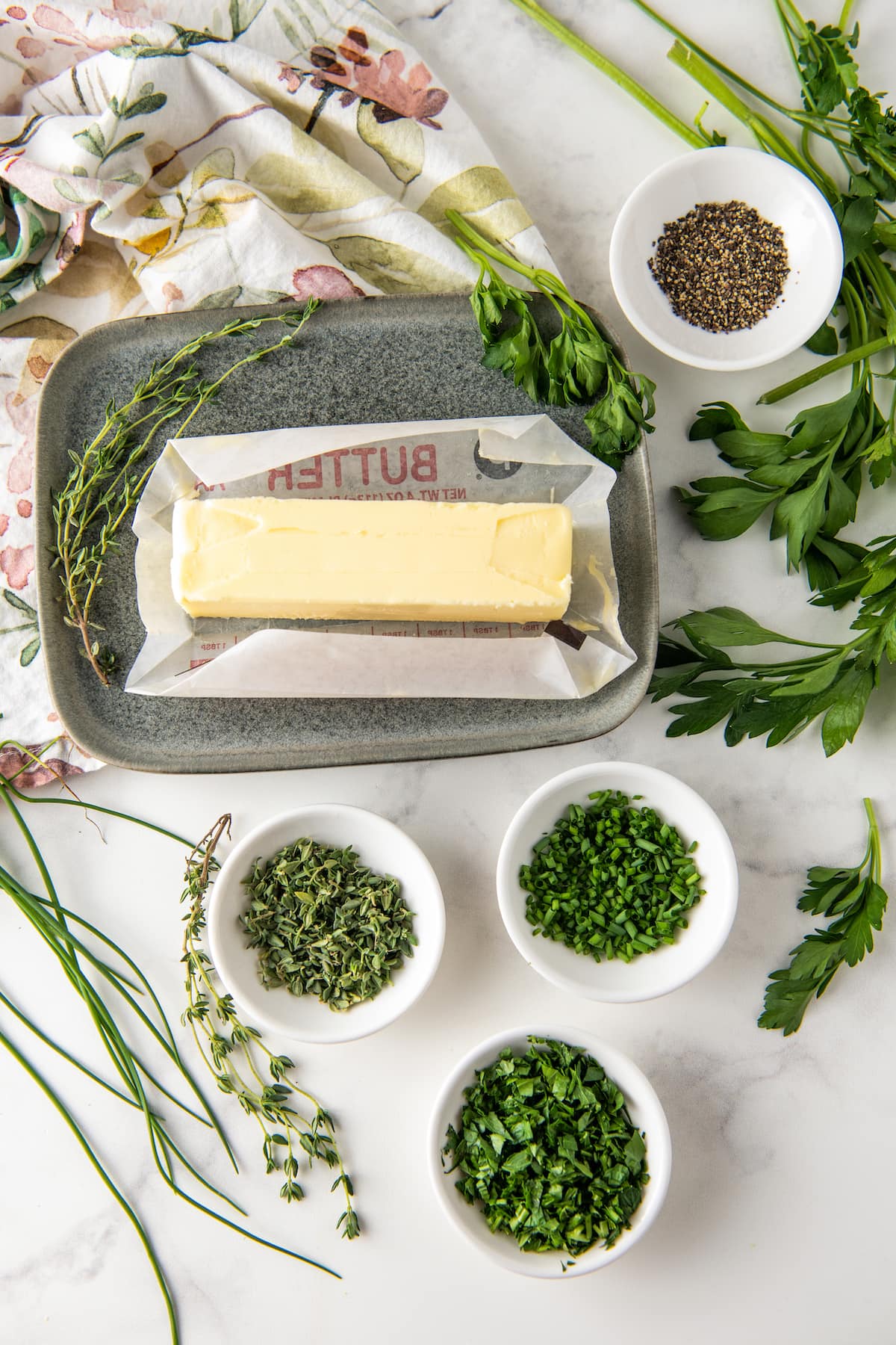 one stick of unwrapped buter alongside ramekins with chopped fresh herbs