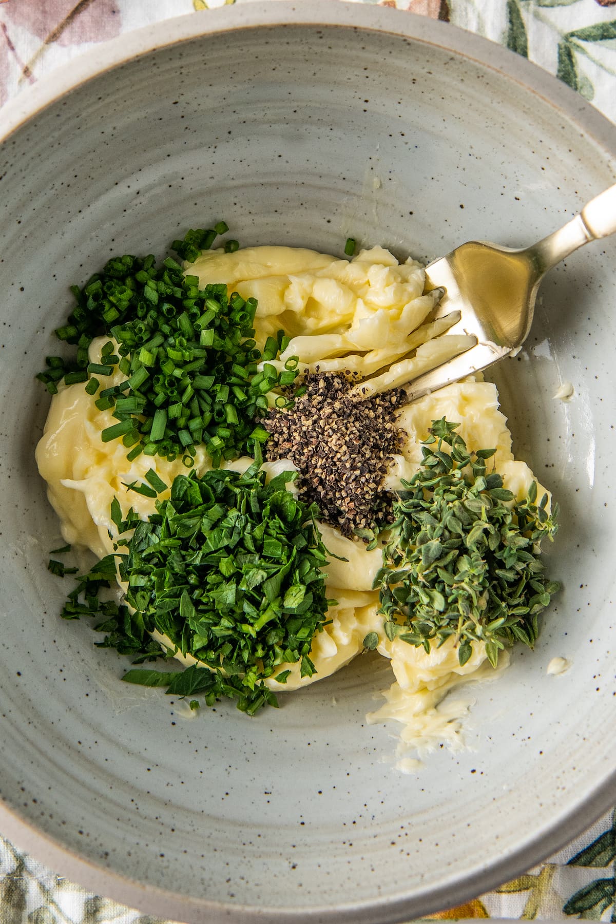 adding chopped fresh herbs to whipped butter in a bowl with a fork