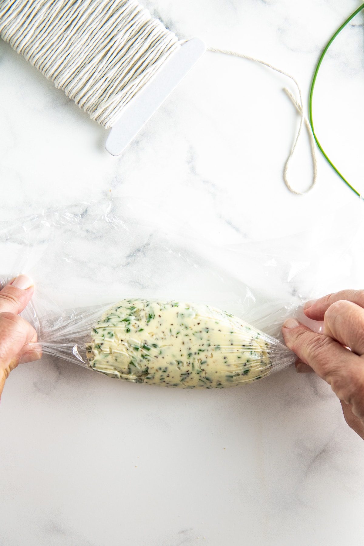 two hands using plastic wrap to wrap herb but ter into a log