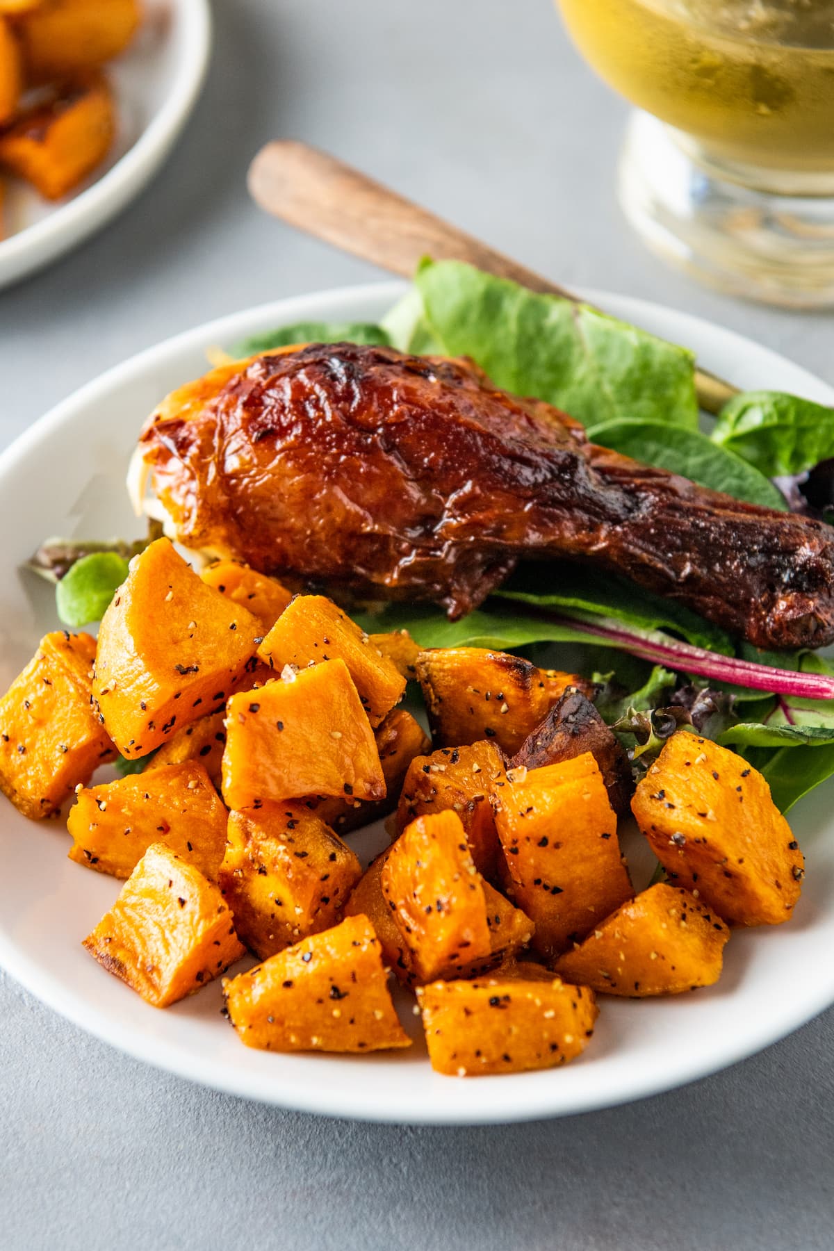 a sweet potato side dish next to a chicken leg and salad on a plate