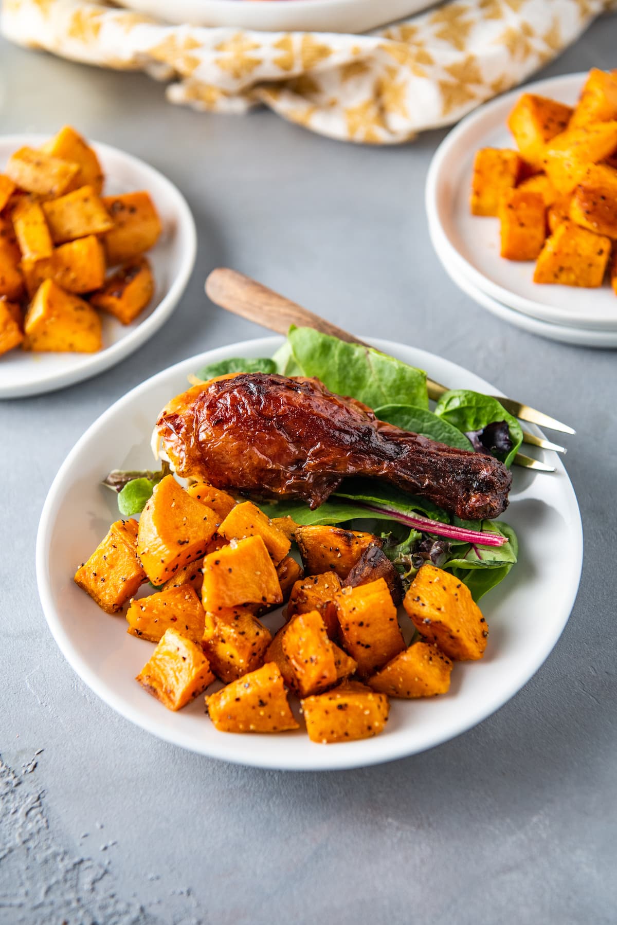 a sweet potato side dish next to a chicken leg and salad on a plate