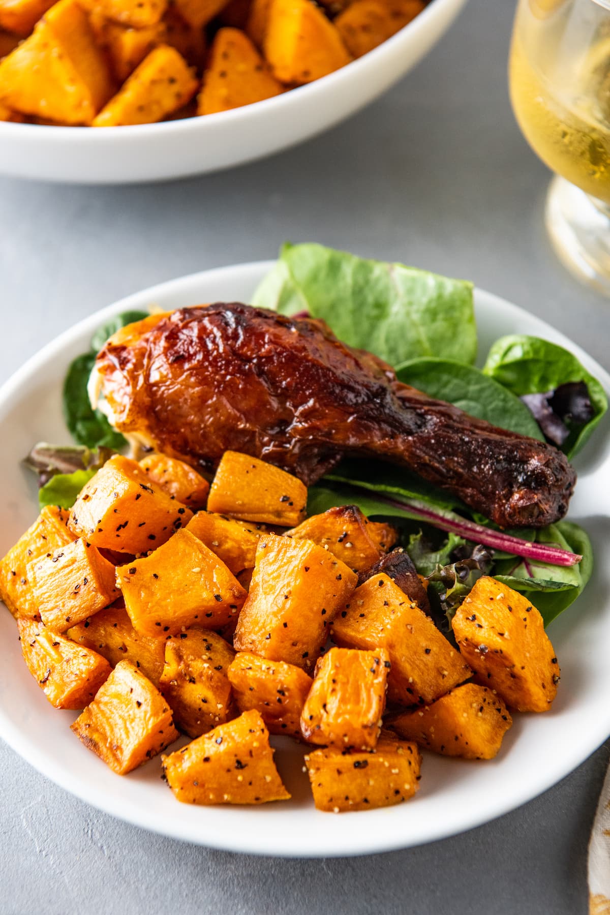 a sweet potato side dish next to a chicken leg and salad on a plate