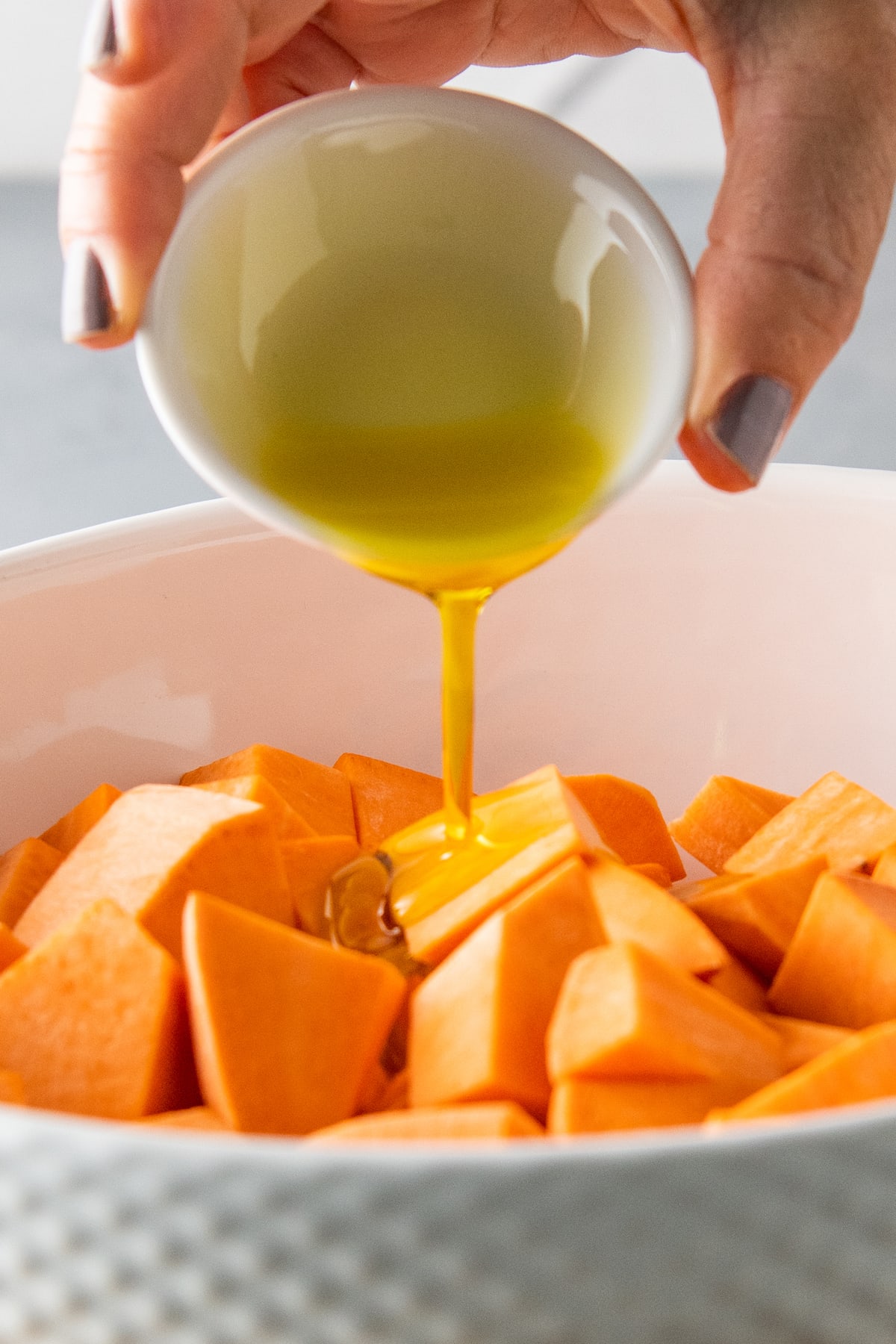 pouring olive oil on to cubed sweet potatoes