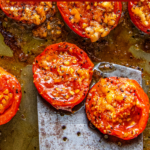 Roasted tomatoes on a baking sheet being scooped up with a spatula.