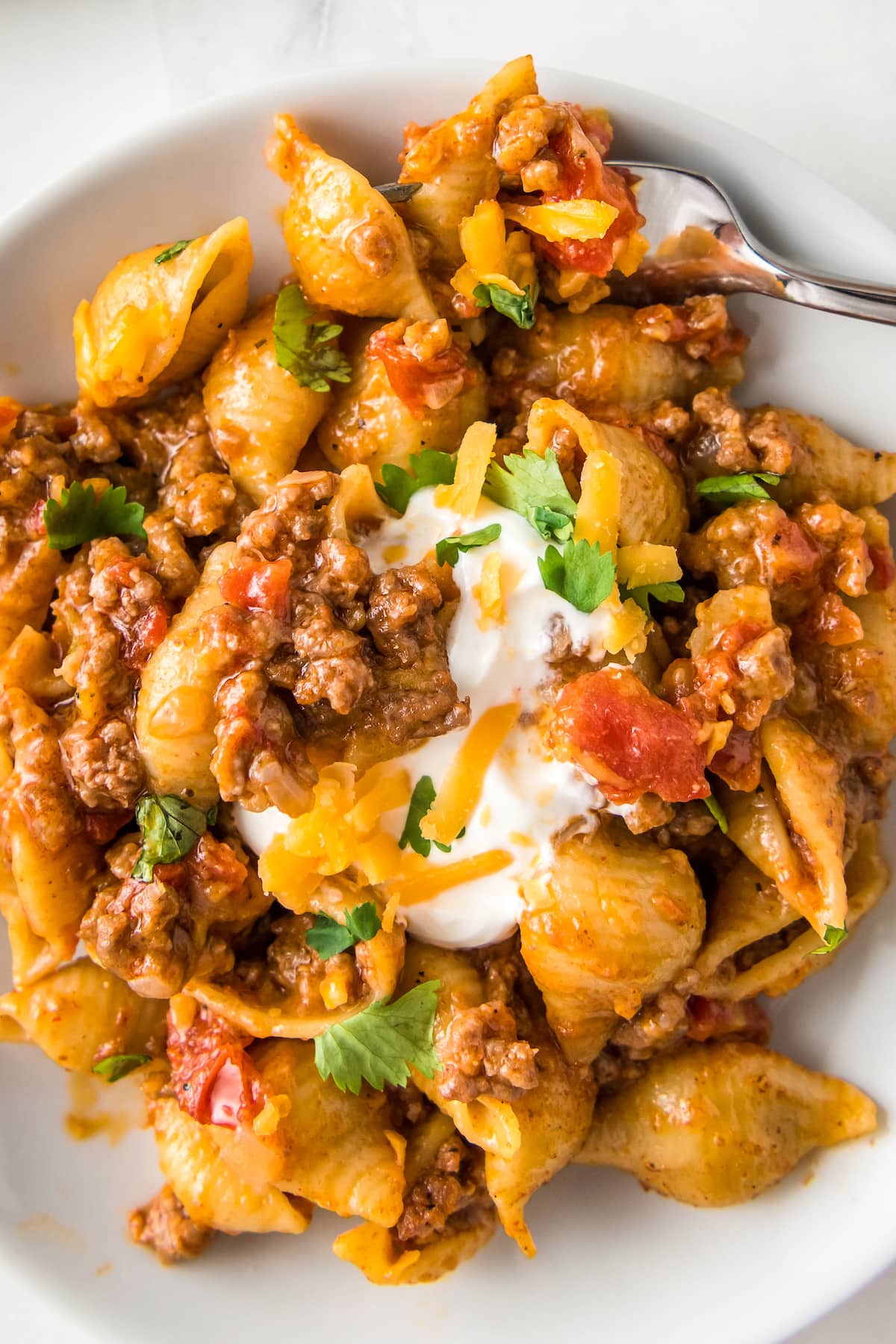 close up of a taco pasta dish with shells, tomato sauce, ground beef, and cheese