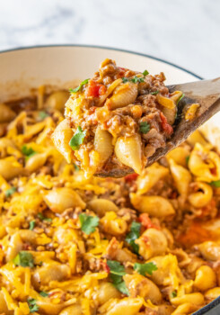 a wooden spoon in a pot with taco pasta made with shells, ground beef, and tomatoes