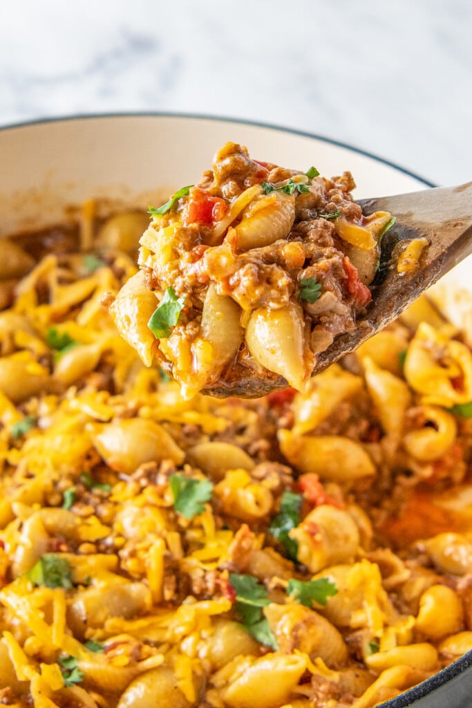 a wooden spoon in a pot with taco pasta made with shells, ground beef, and tomatoes