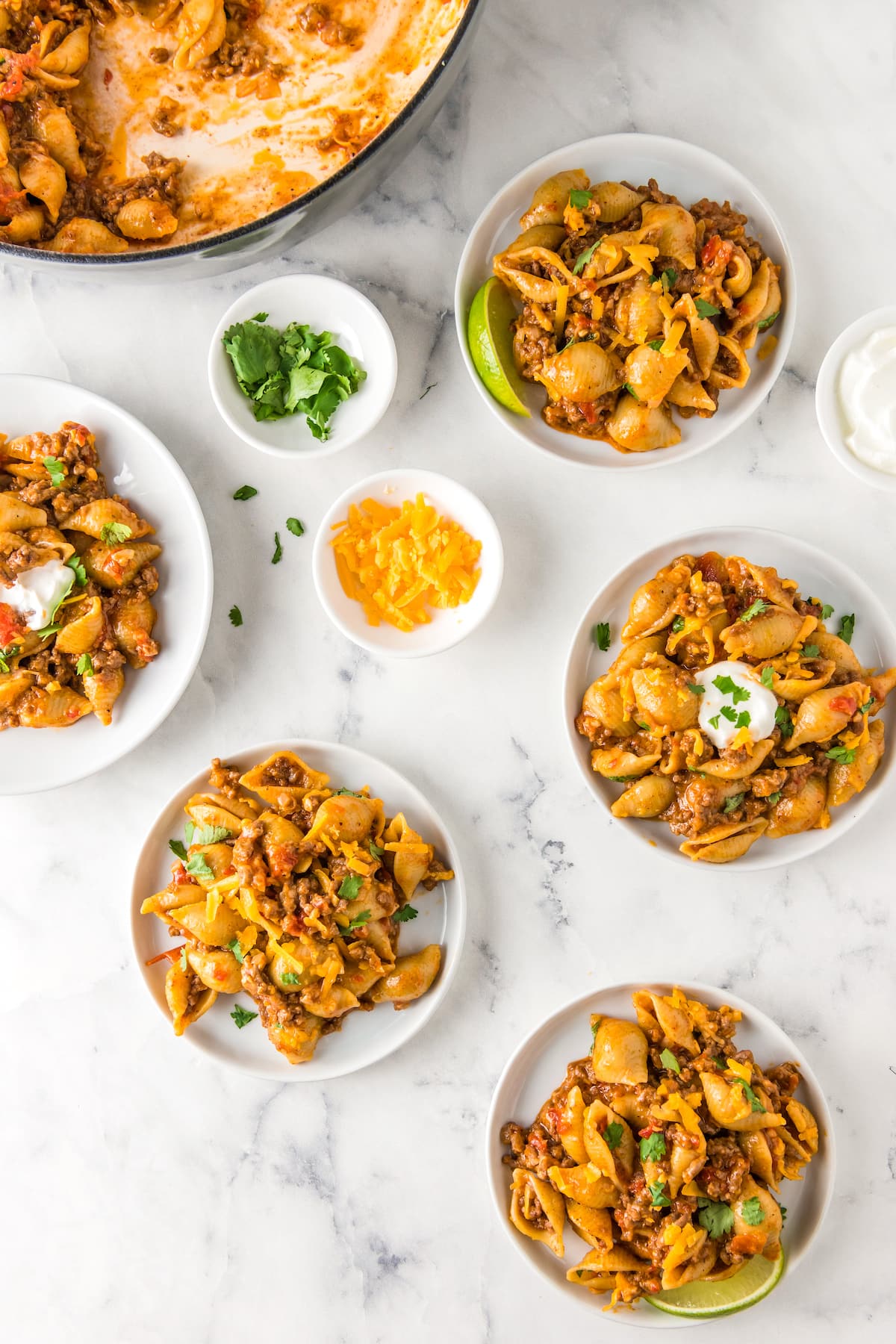 multiple plated pasta dishes with ground beef, shells, cheese, green onions, and tomatoes