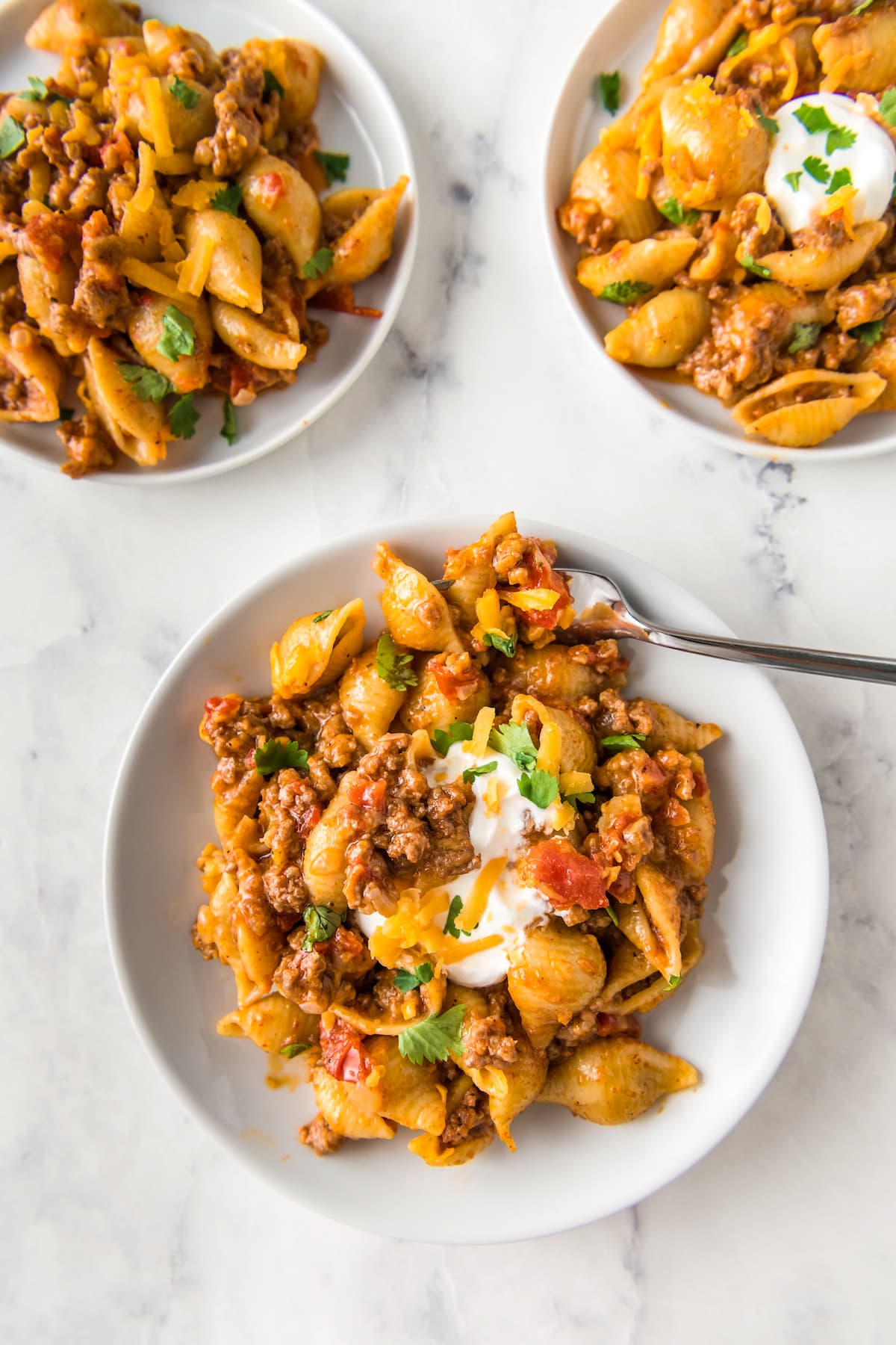 plated pasta dish with ground beef, shells, cheese, green onions, and tomatoes