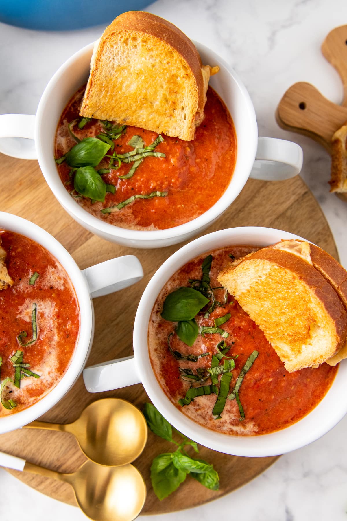 three bowls of tomato basil soup with grilled cheese in the bowls