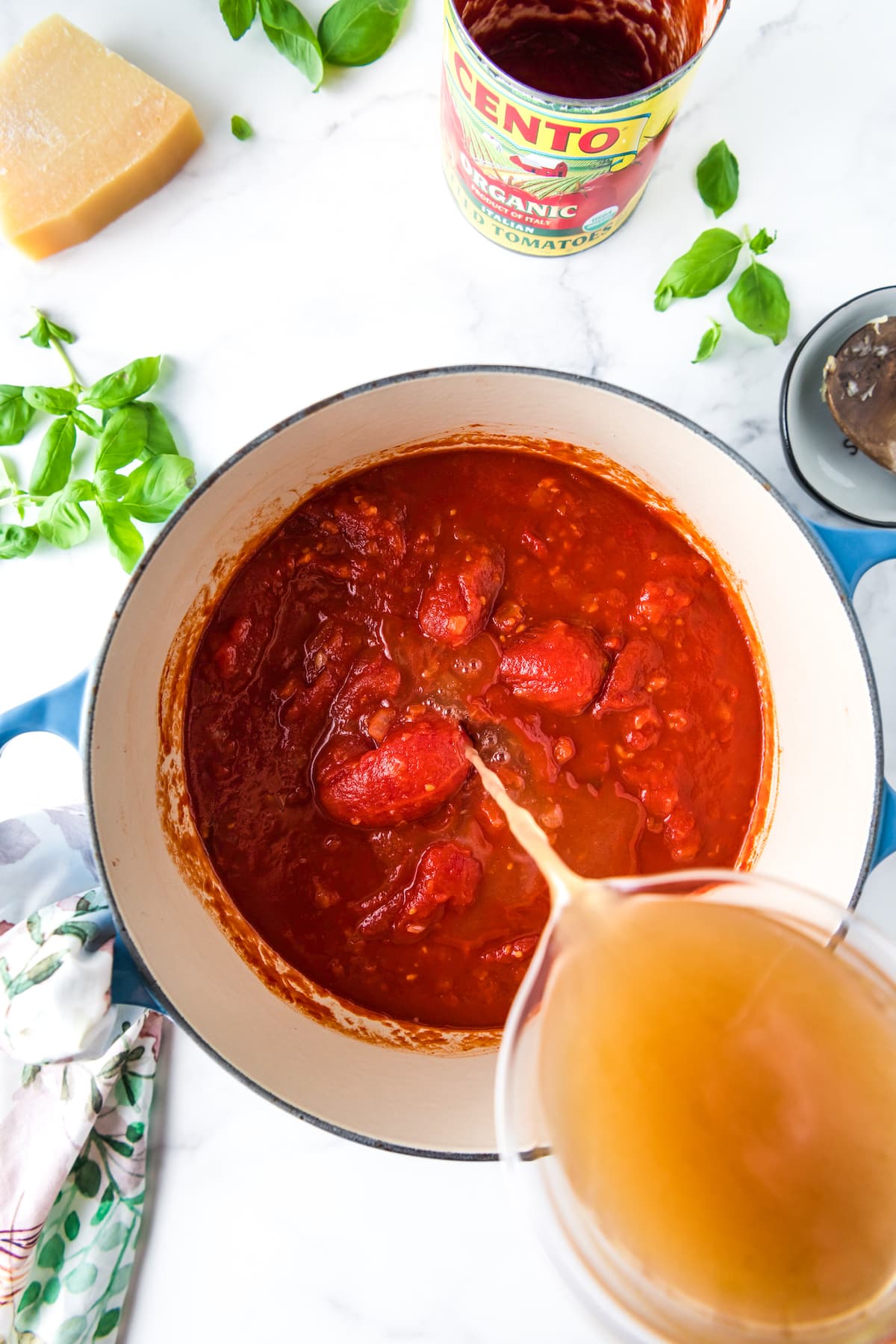 pouring stock into a pot with a tomatoes and tomato sauce