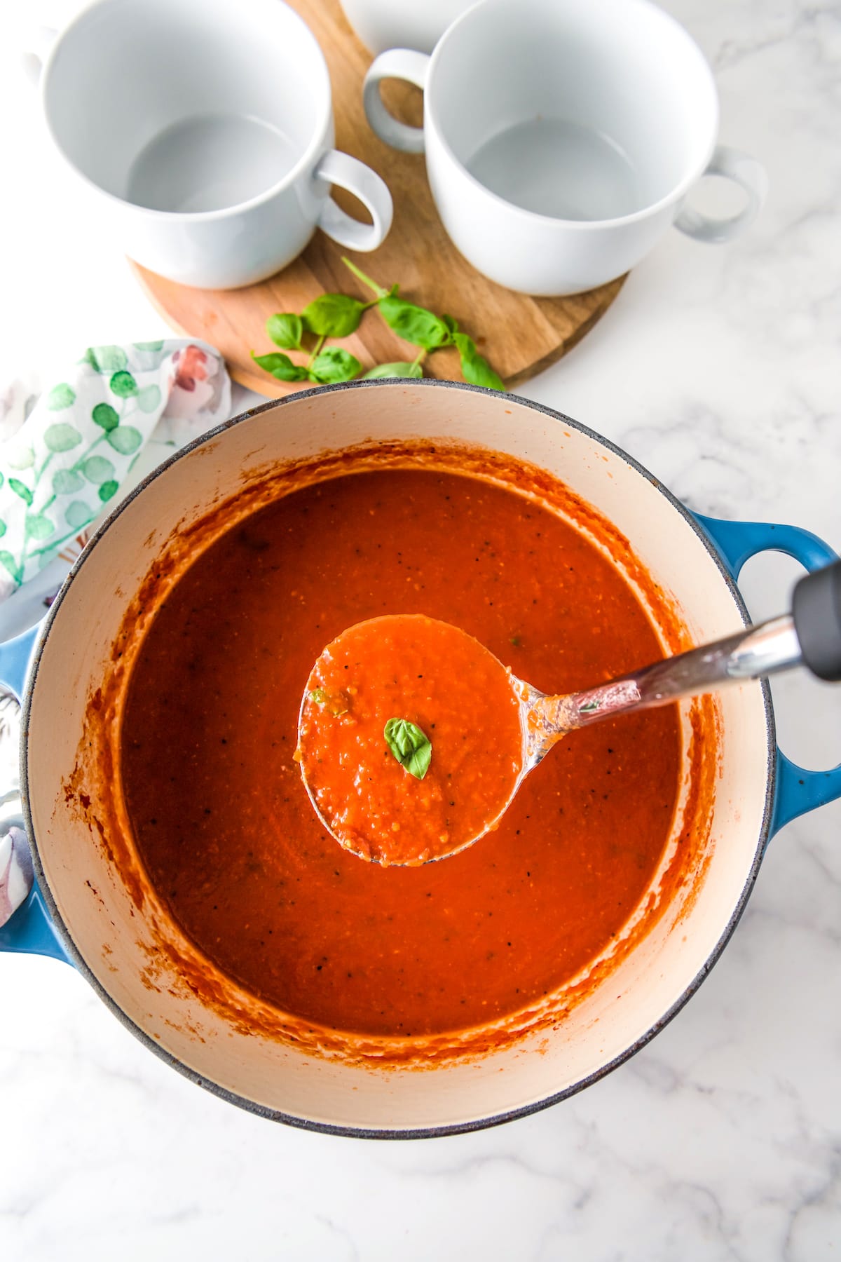 a ladle and large pot with tomato basil soup