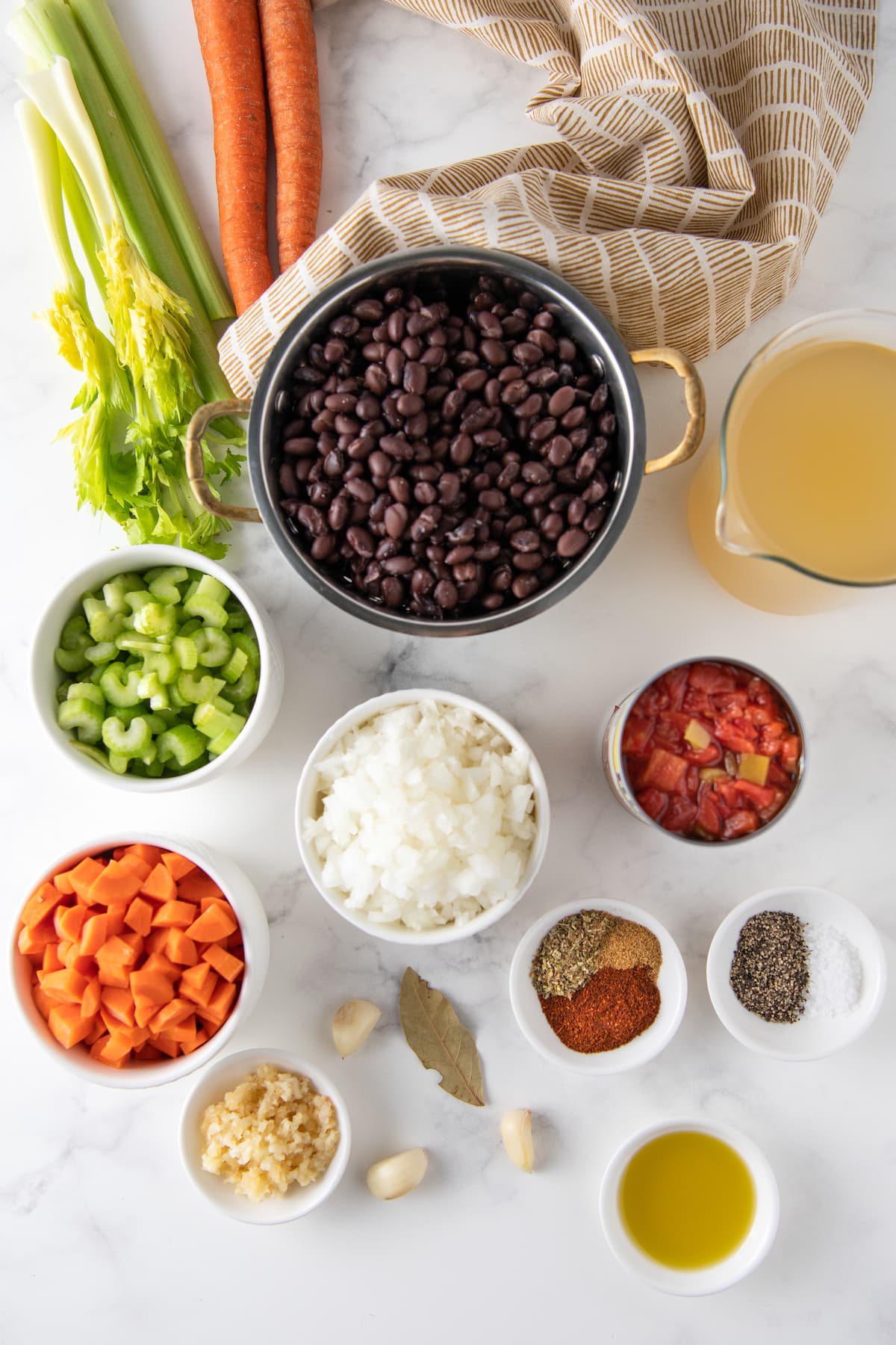 various ingredients to make carrot black bean soup like black beans, diced vegetables, and seasonings in different prep bowls