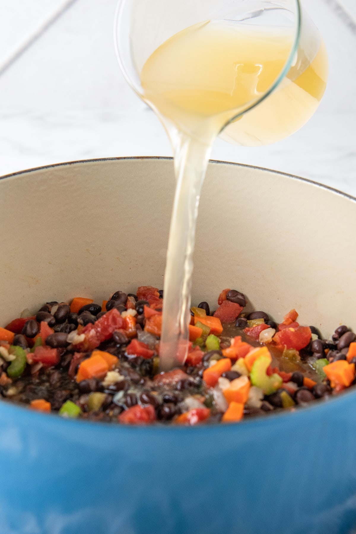 pouring broth into a pot with black beans and diced vegetables