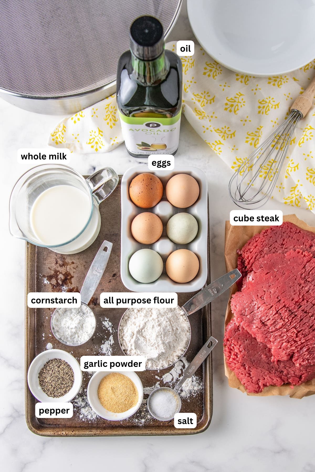 The ingredients for chicken fried steak recipe in order from top to bottom: oil, whole milk, eggs, cube steak, cornstarch, all purpose flour, pepper, garlic powder, salt.