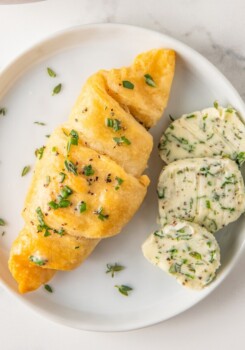 a crescent roll on a plate with slices of herb butter