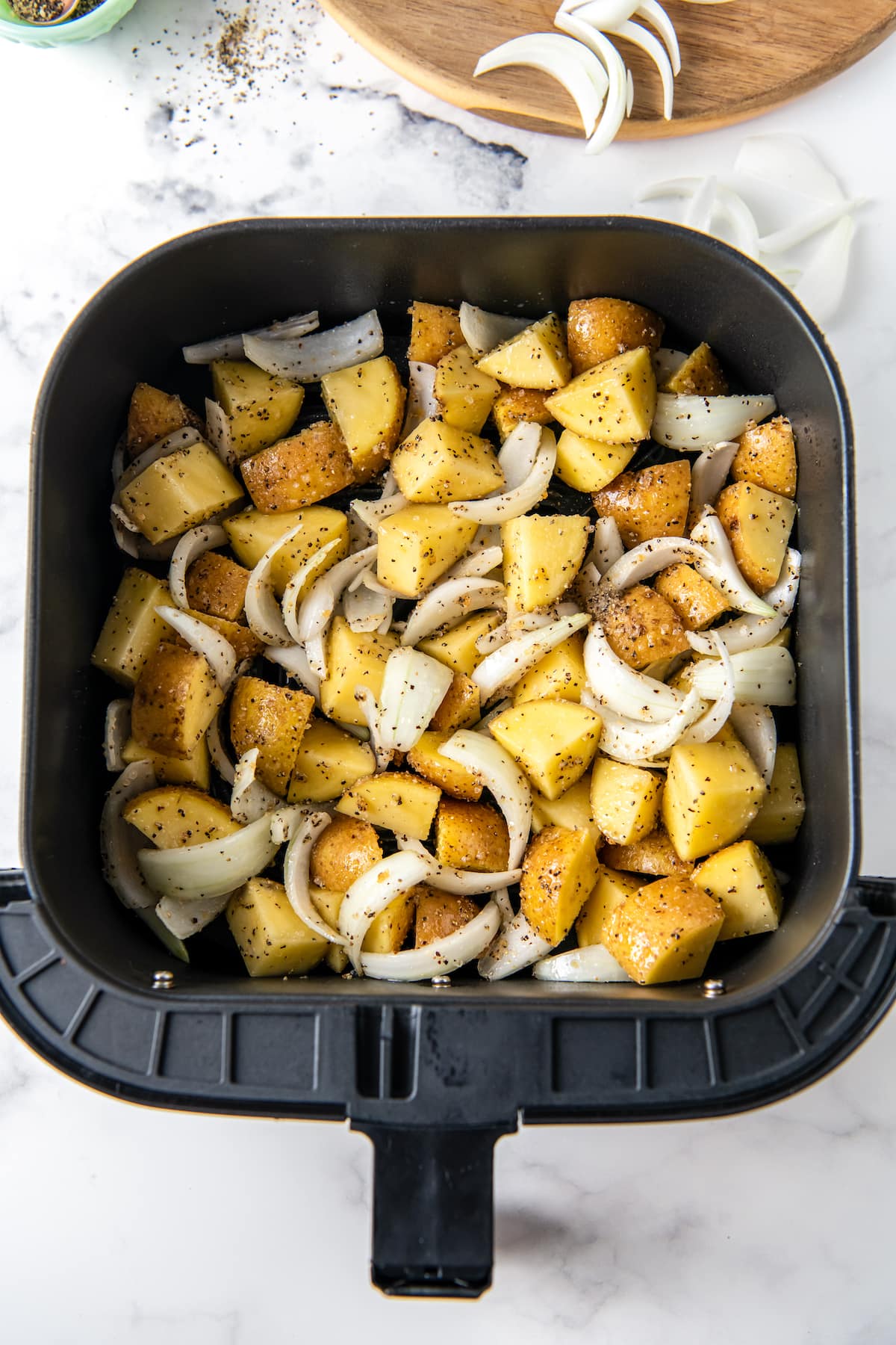 Chopped potatoes and onions in an air fryer.
