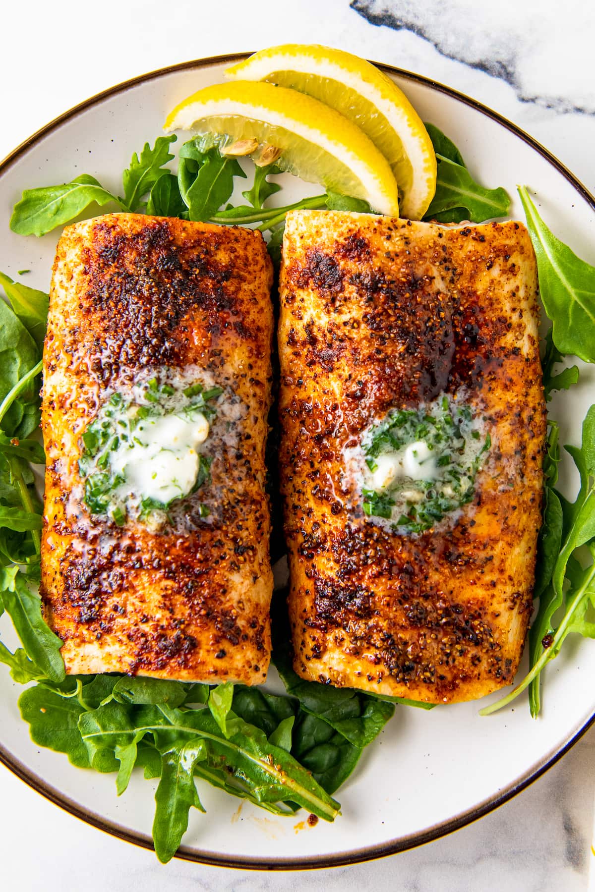 Buttery mahi mahi filets are placed on top of a bed of arugula with fresh lemon wedges. 