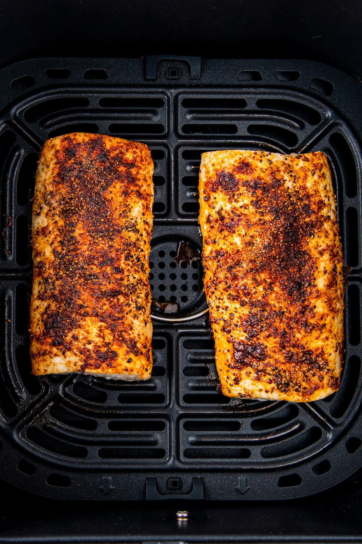 Two fully cooked fish filets are in an air fryer basket. 