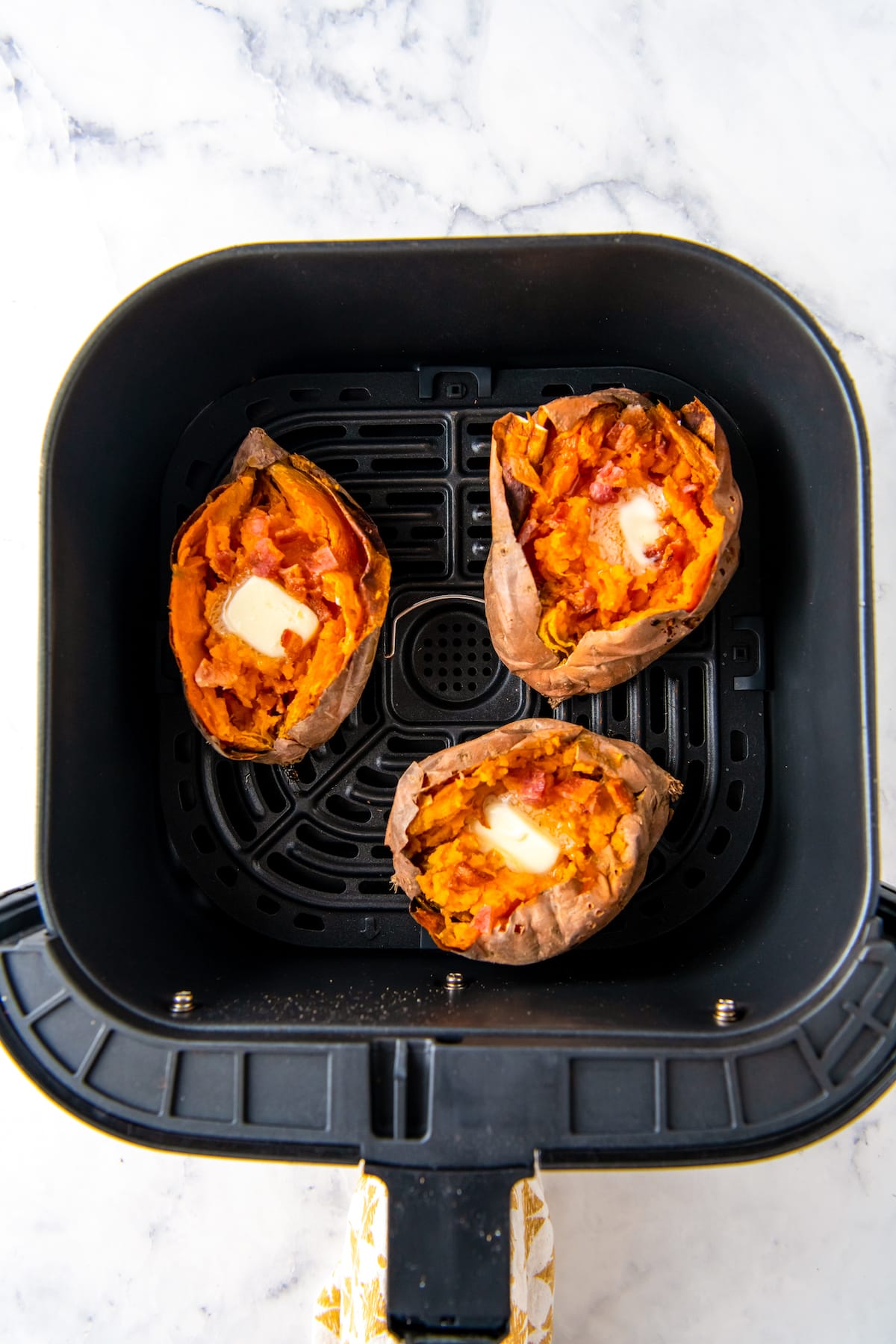 three sweet potatoes in an air fryer cut open with butter on top